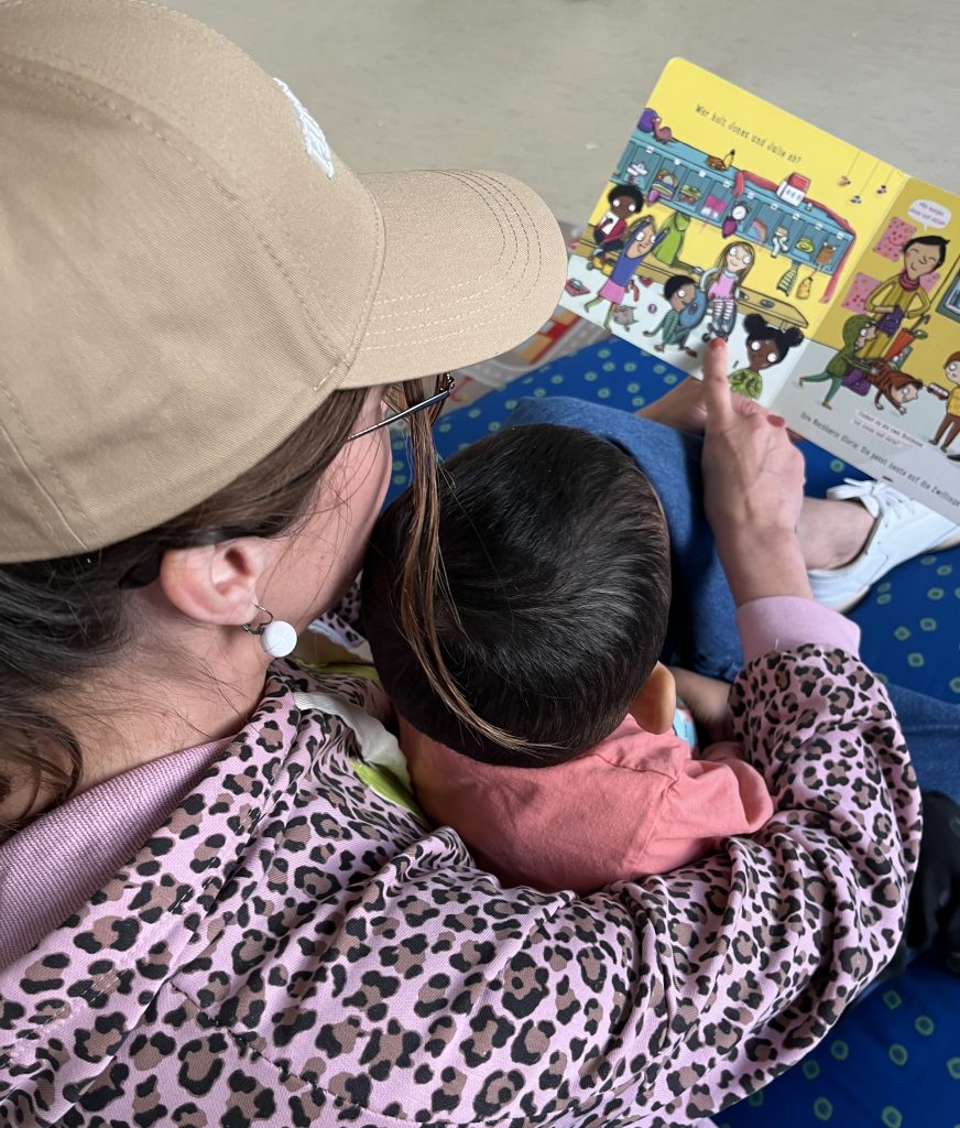 Eine Erzieherin hat ein Kind auf dem Schoß und sie schauen gemeinsam in ein Kinderbuch. 